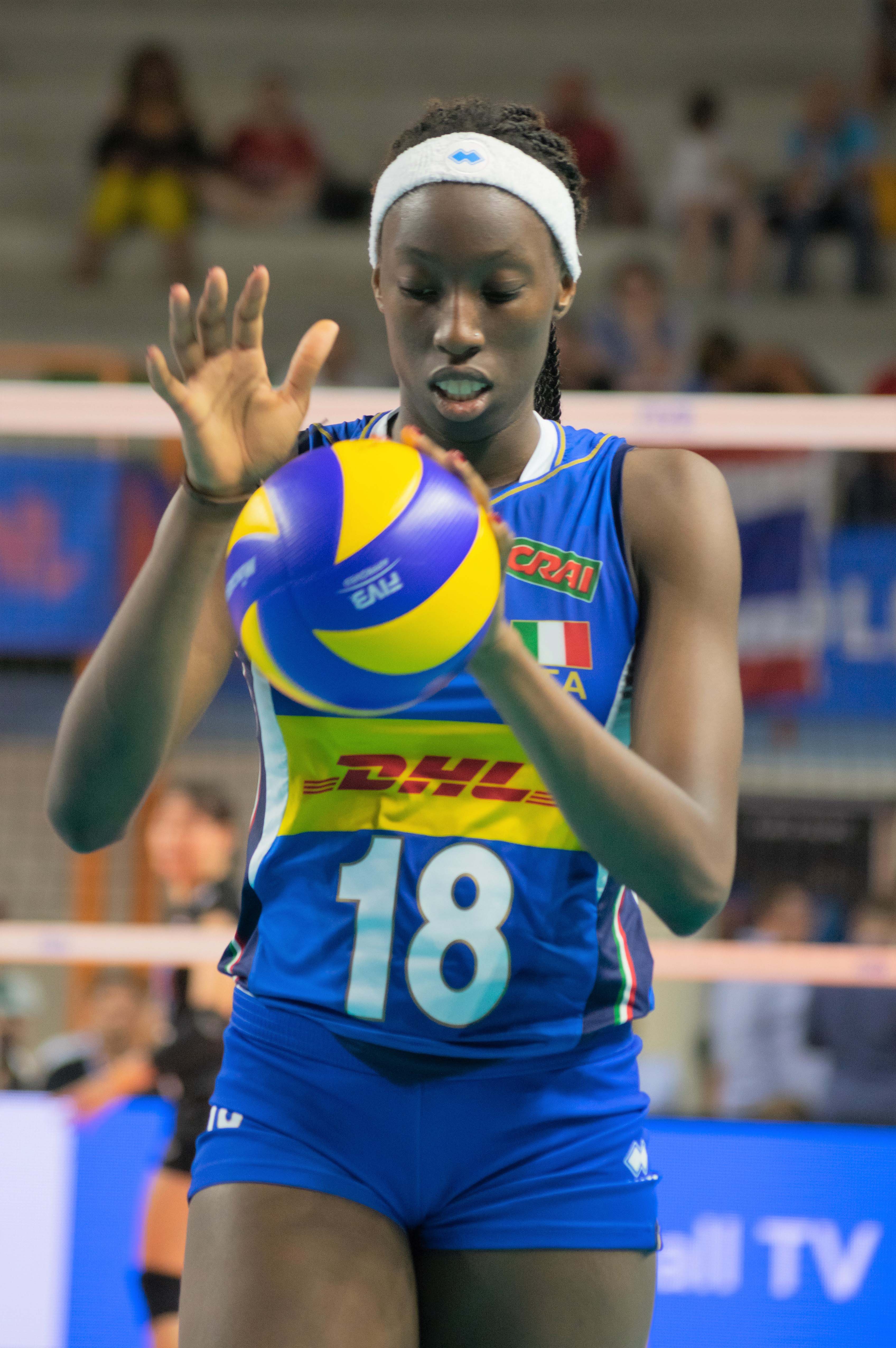 A female volleyball player seen from the front holding a volleyball in one hand about to hit it down with the other.