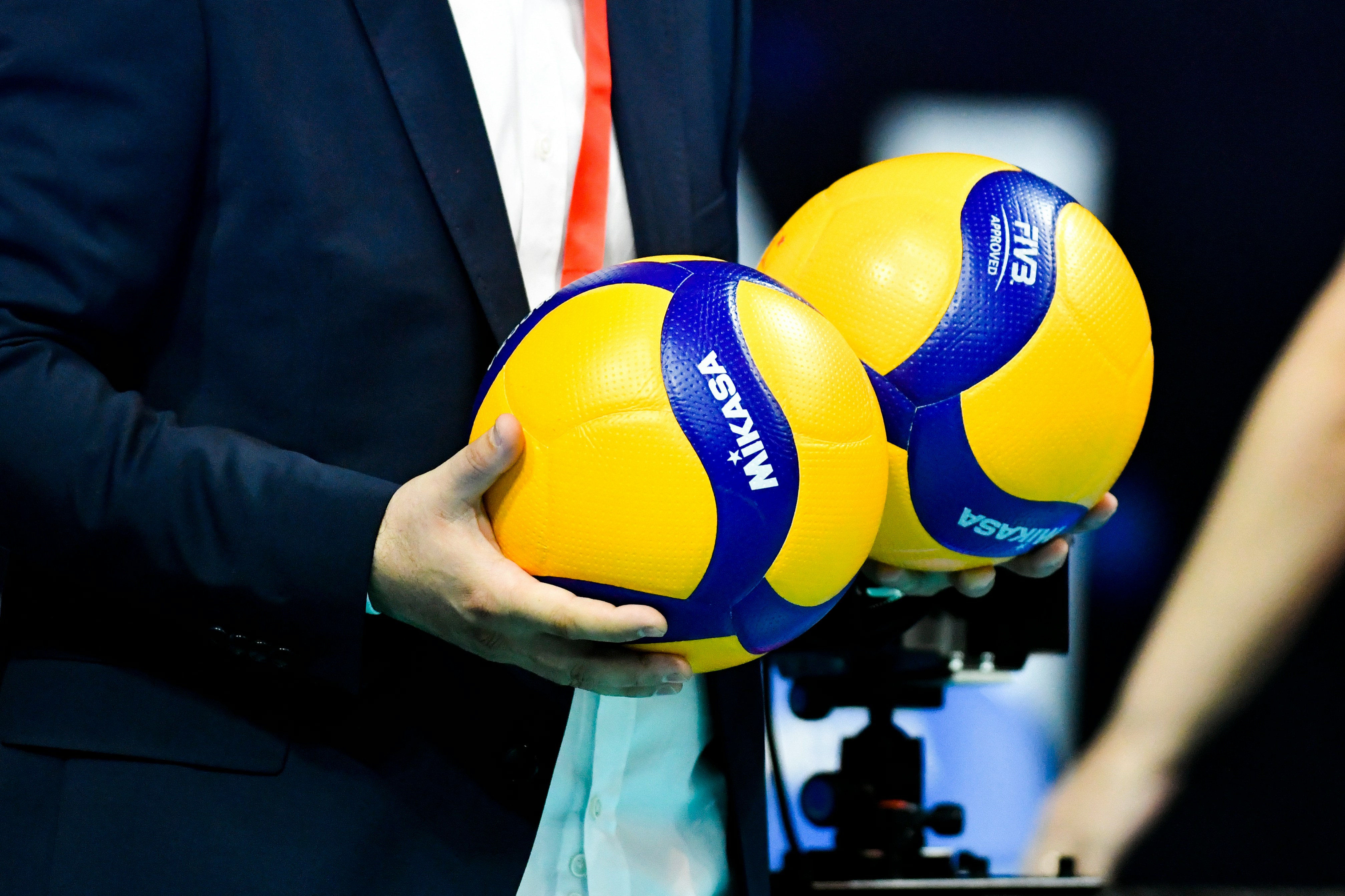 A man seen from chest down holding two yellow and blue volleyballs in his hand.