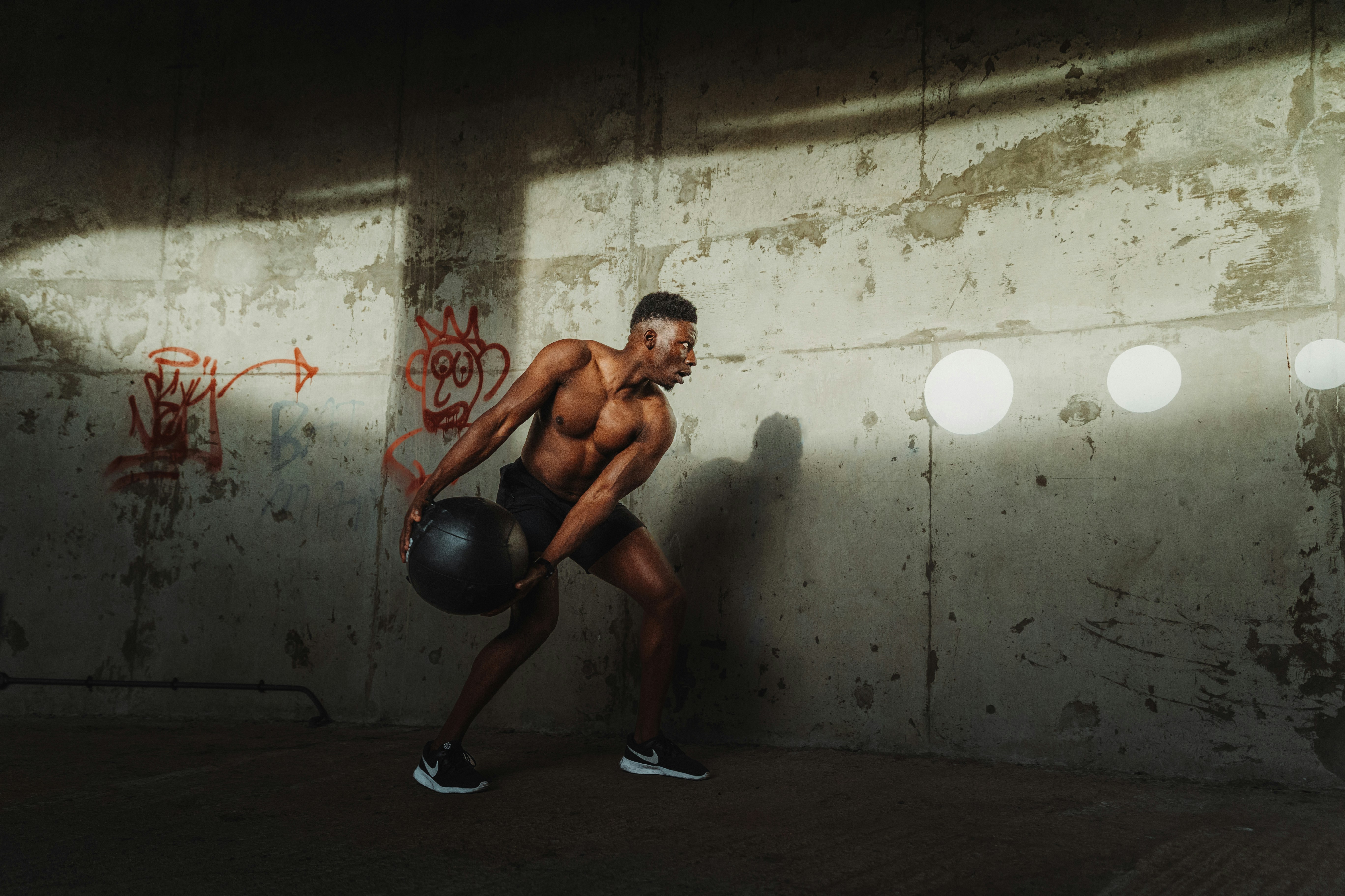 A man seen holding a medicine ball about to throw it against a concrete wall.
